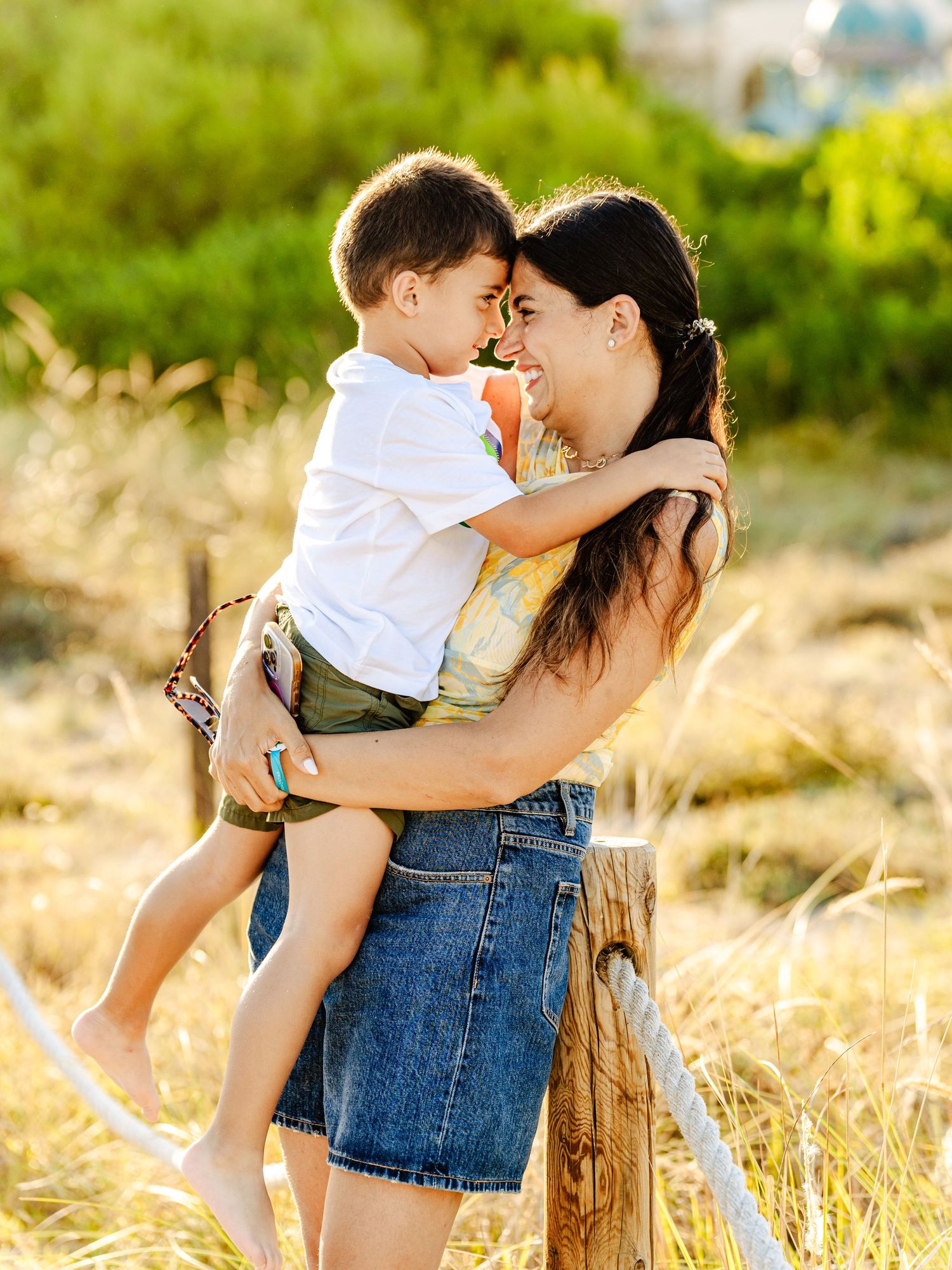 Loving mother holding young son close as they touch foreheads in golden sunlit field.