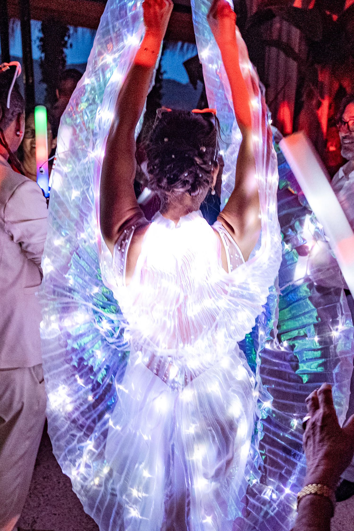 Dancer wearing glowing white LED wings costume entertaining guests at a vibrant nighttime wedding reception.