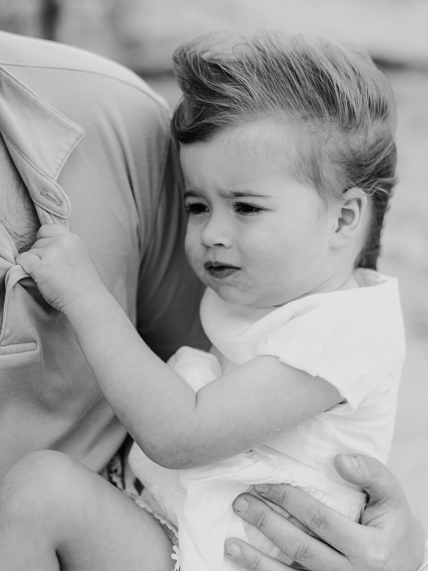 Black and white close-up portrait of an adorable toddler with stylish hair at the beach.