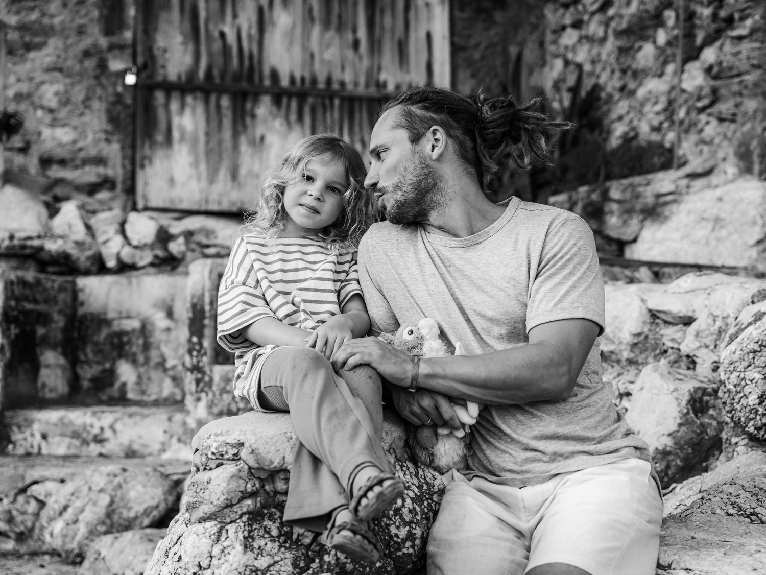 Black and white photo of father and young daughter sharing tender moment while sitting on stone steps.