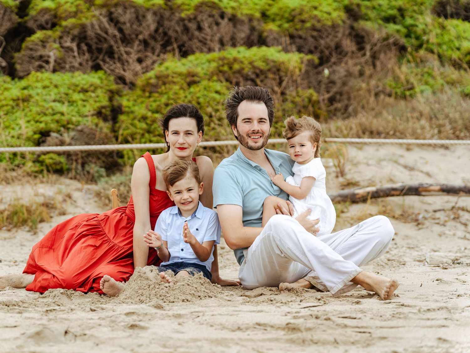 Family of four enjoying a relaxed beach portrait with two young children, captured during a natural outdoor family photography session.
