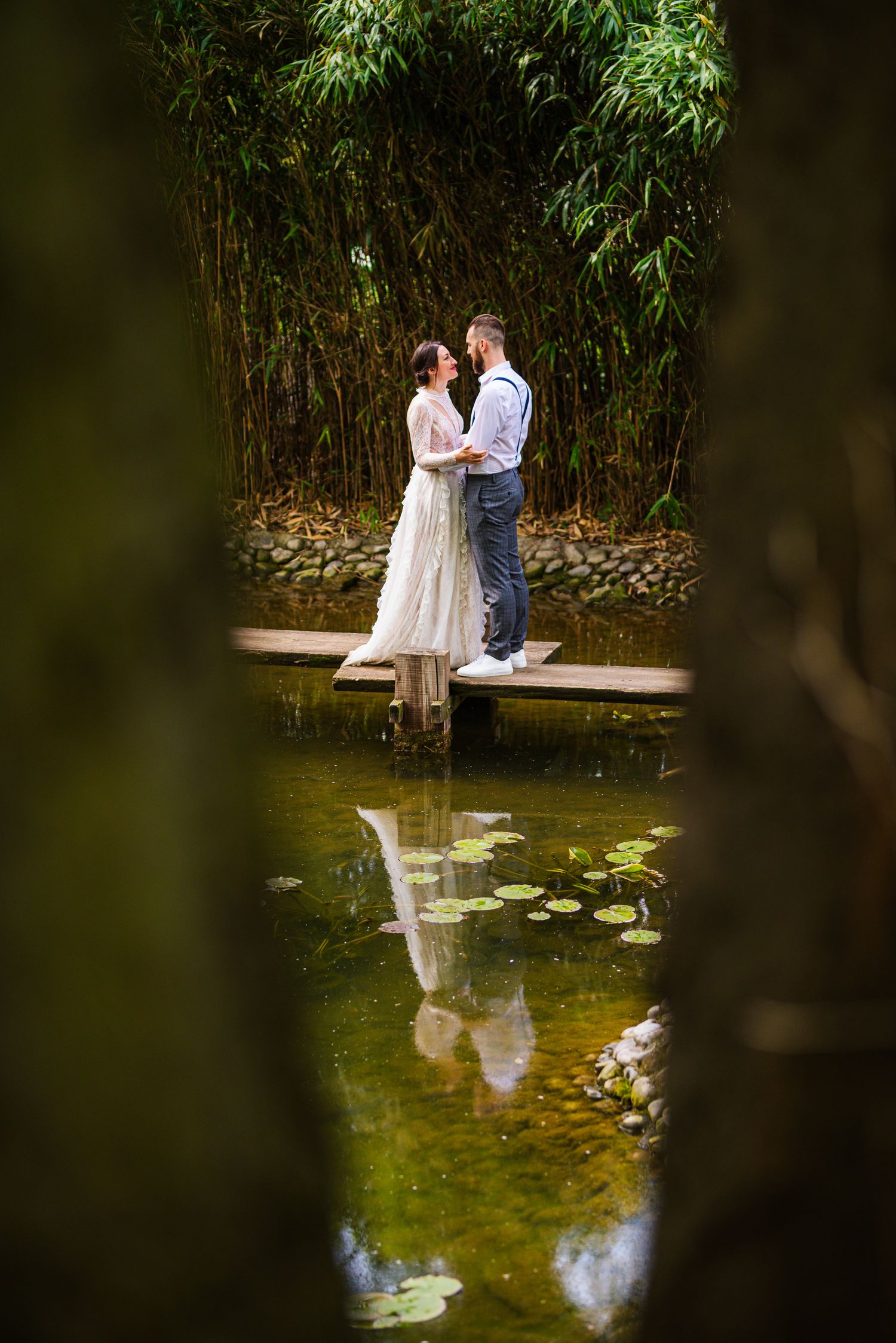 Bride and groom reflected in still water, surrounded by nature - two lives meeting quietly. Herzenshaus Studio, Frankfurt.