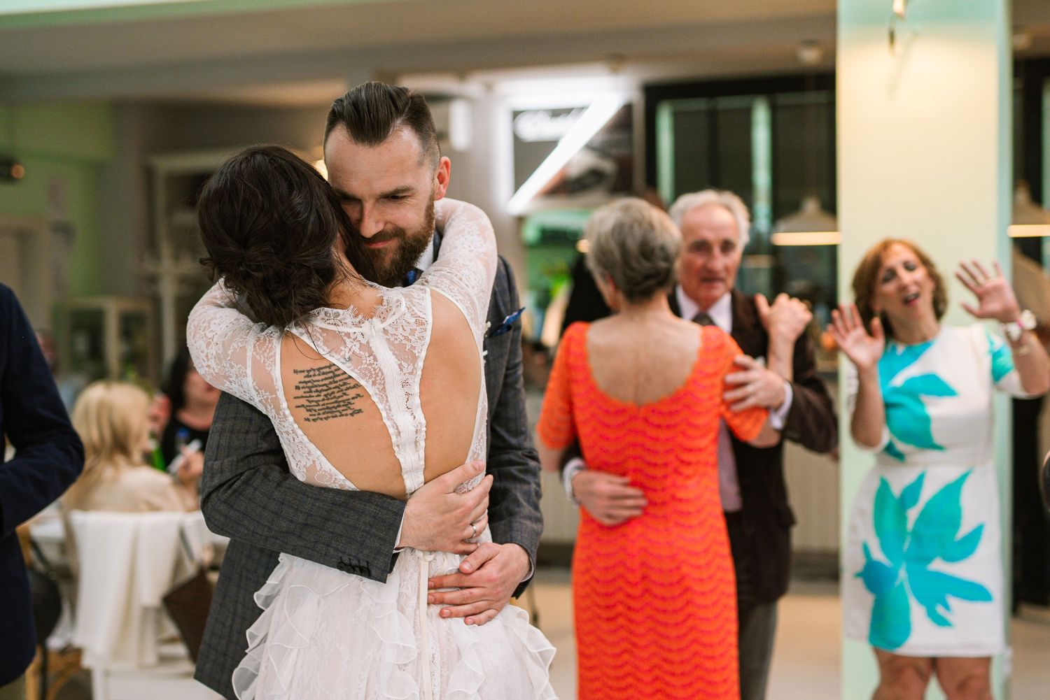 Newlyweds share a warm embrace on the dance floor surrounded by wedding guests.
