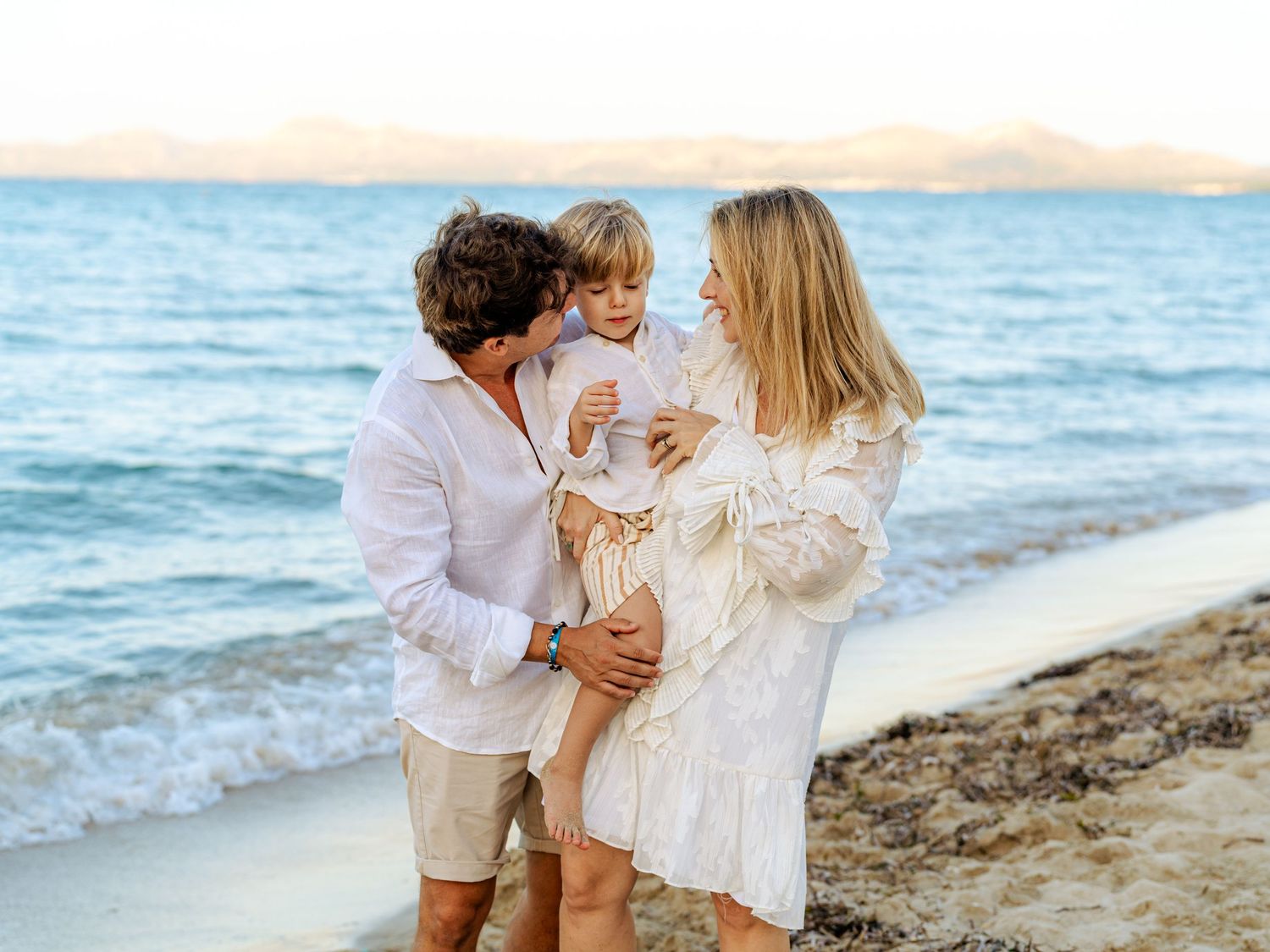 Pregnant mother and father with toddler son on sandy beach.