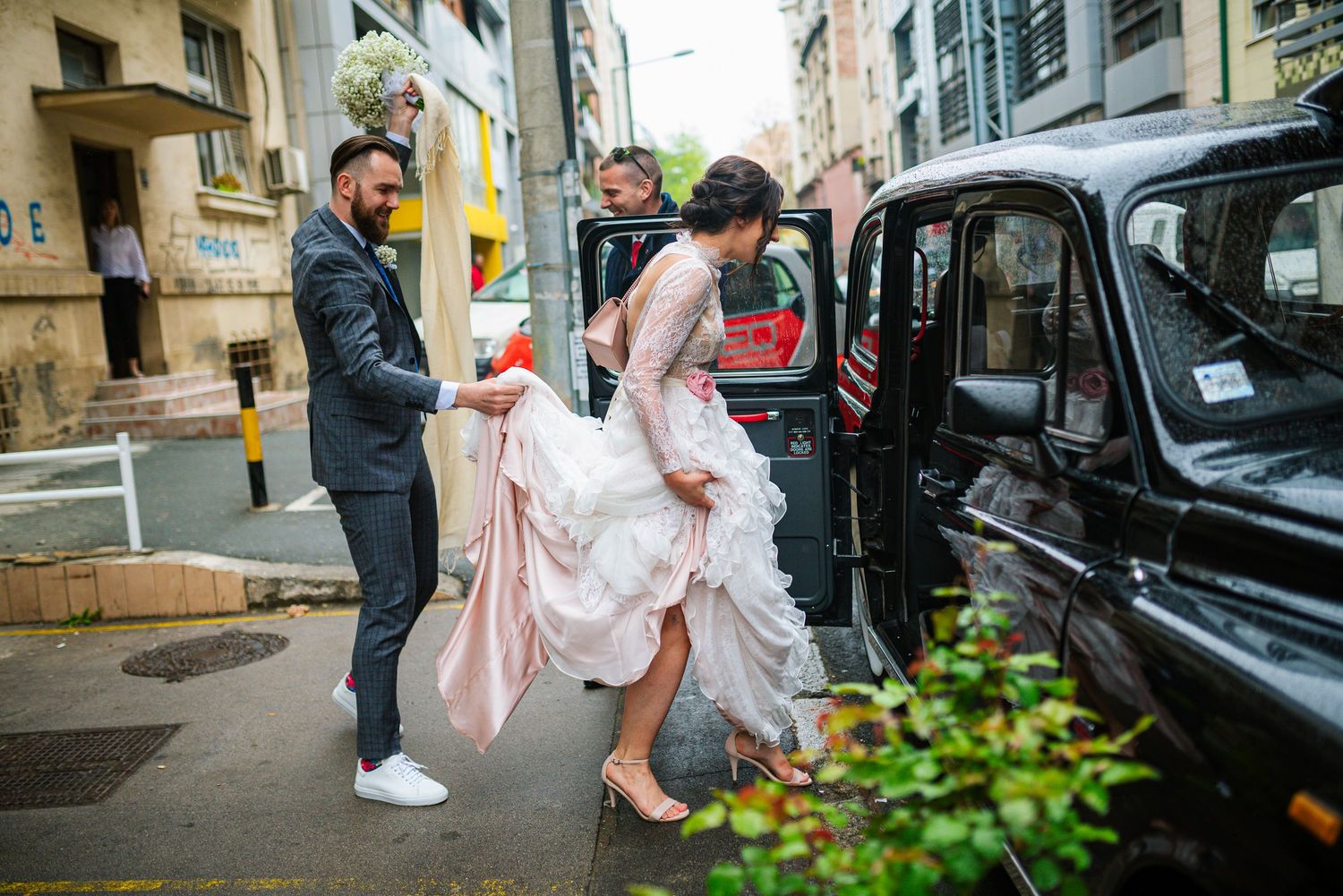Groom helping bride into classic black London taxi cab on wedding day.