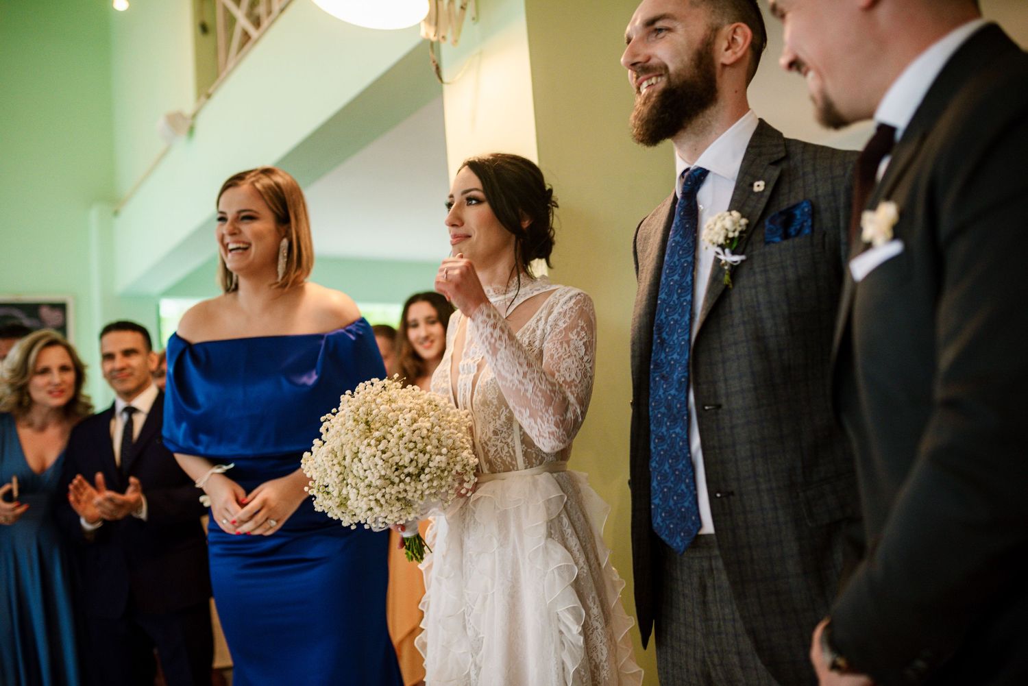 Bride holding baby's breath bouquet stands with bearded groom during wedding ceremony indoors.