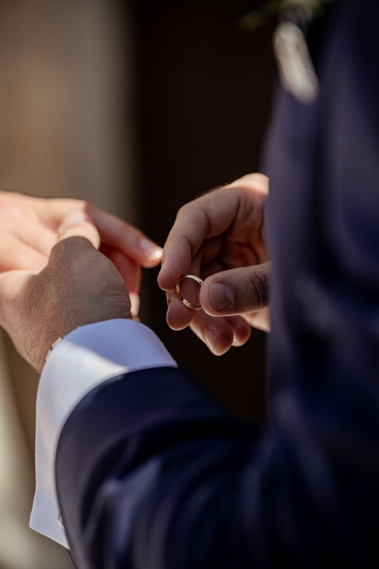 Close-up of groom placing gold wedding ring on brides finger during ring exchange ceremony.