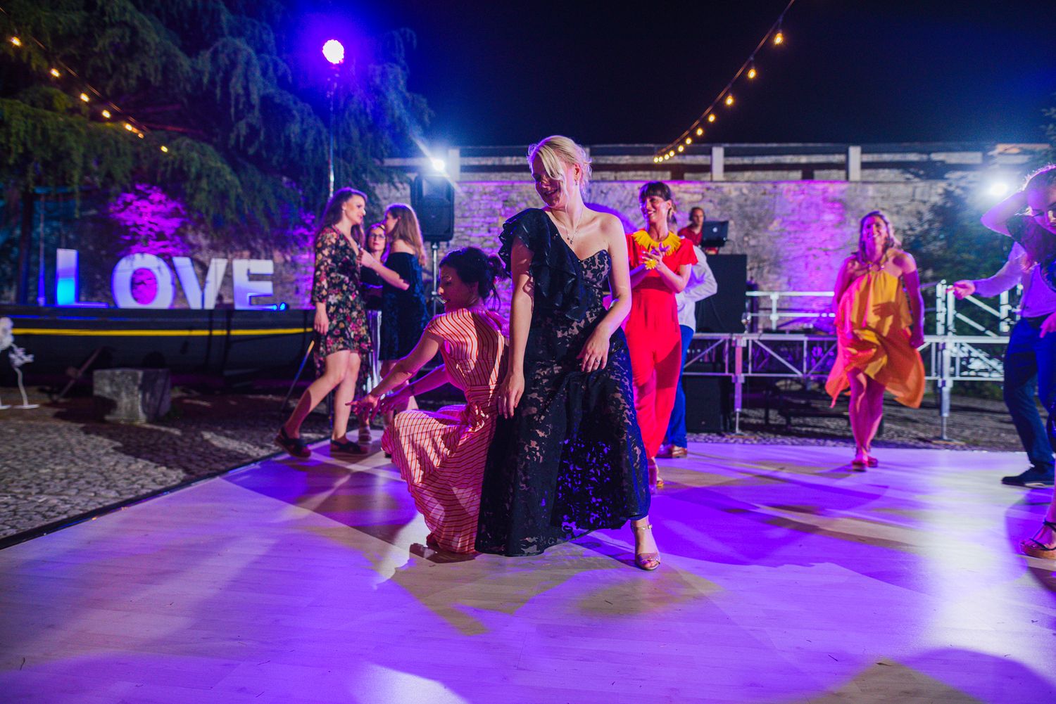 Guests dancing on illuminated outdoor wedding dance floor with LOVE sign at night.