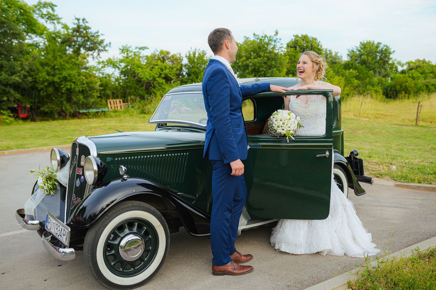 Bride and groom posing beside a vintage black classic car on their wedding day.
