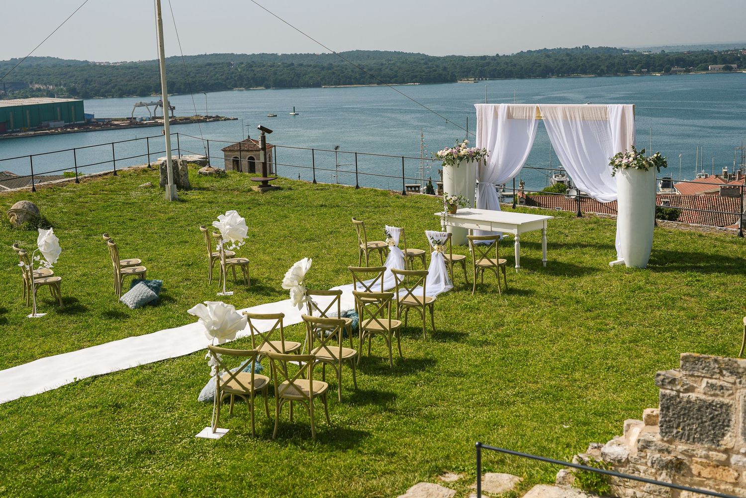 Romantic outdoor wedding ceremony setup overlooking scenic waterfront with white floral arch.