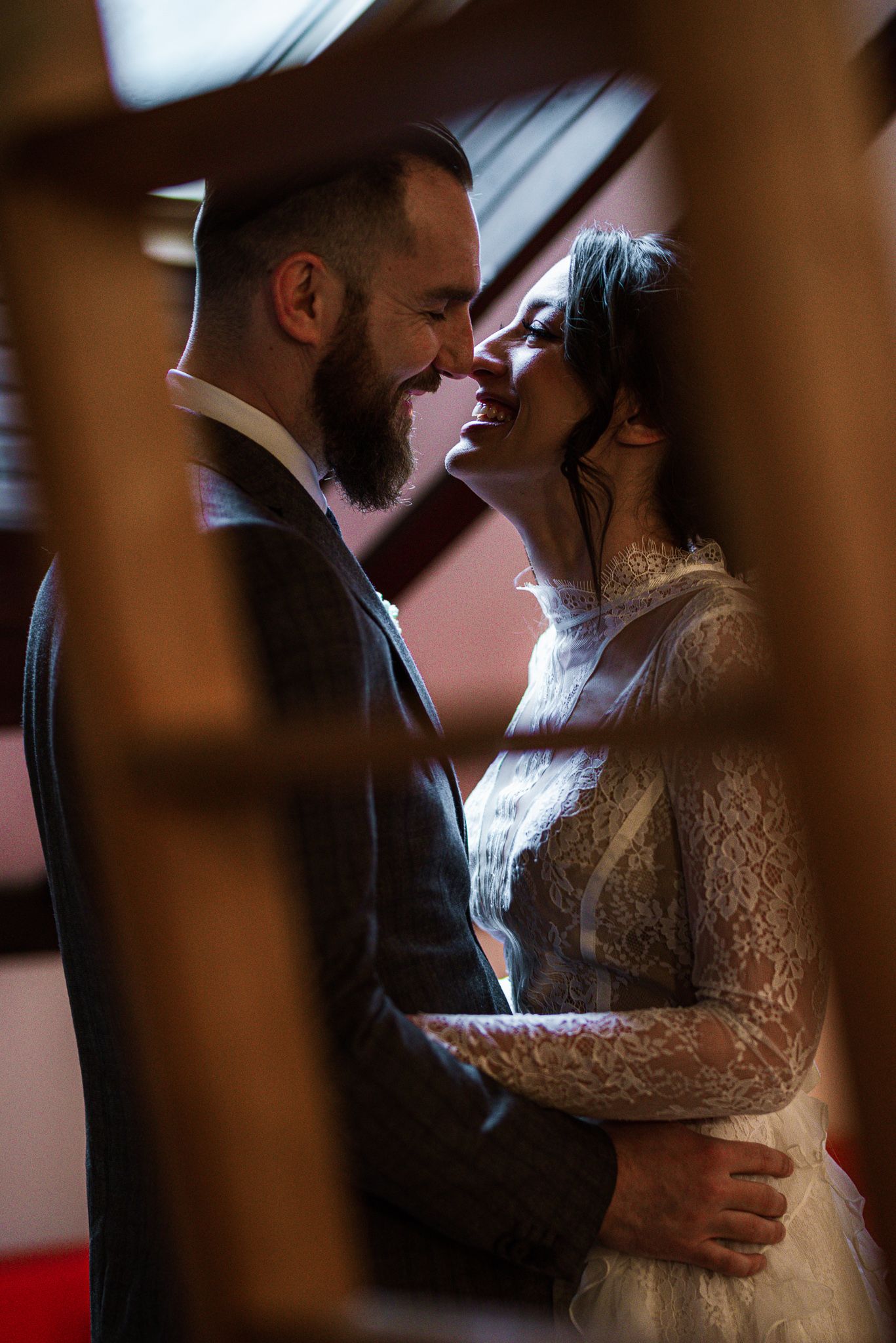 Romantic bride and groom sharing an intimate moment, nearly kissing in a warmly lit attic space.