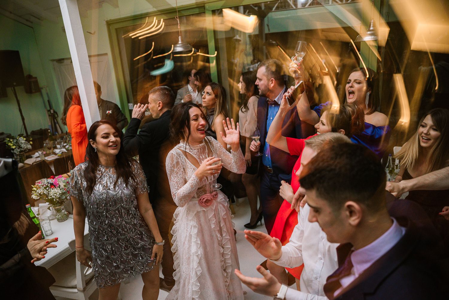 Bride in lace gown dances joyfully with wedding guests on the reception dance floor.