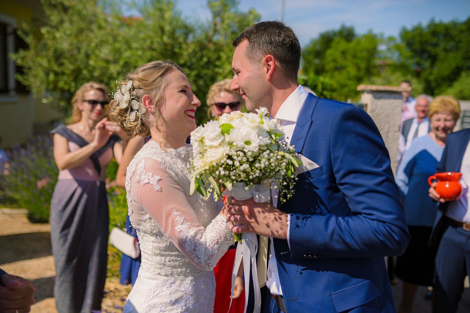 Smiling bride and groom sharing joyful moment holding white bouquet during outdoor wedding ceremony.