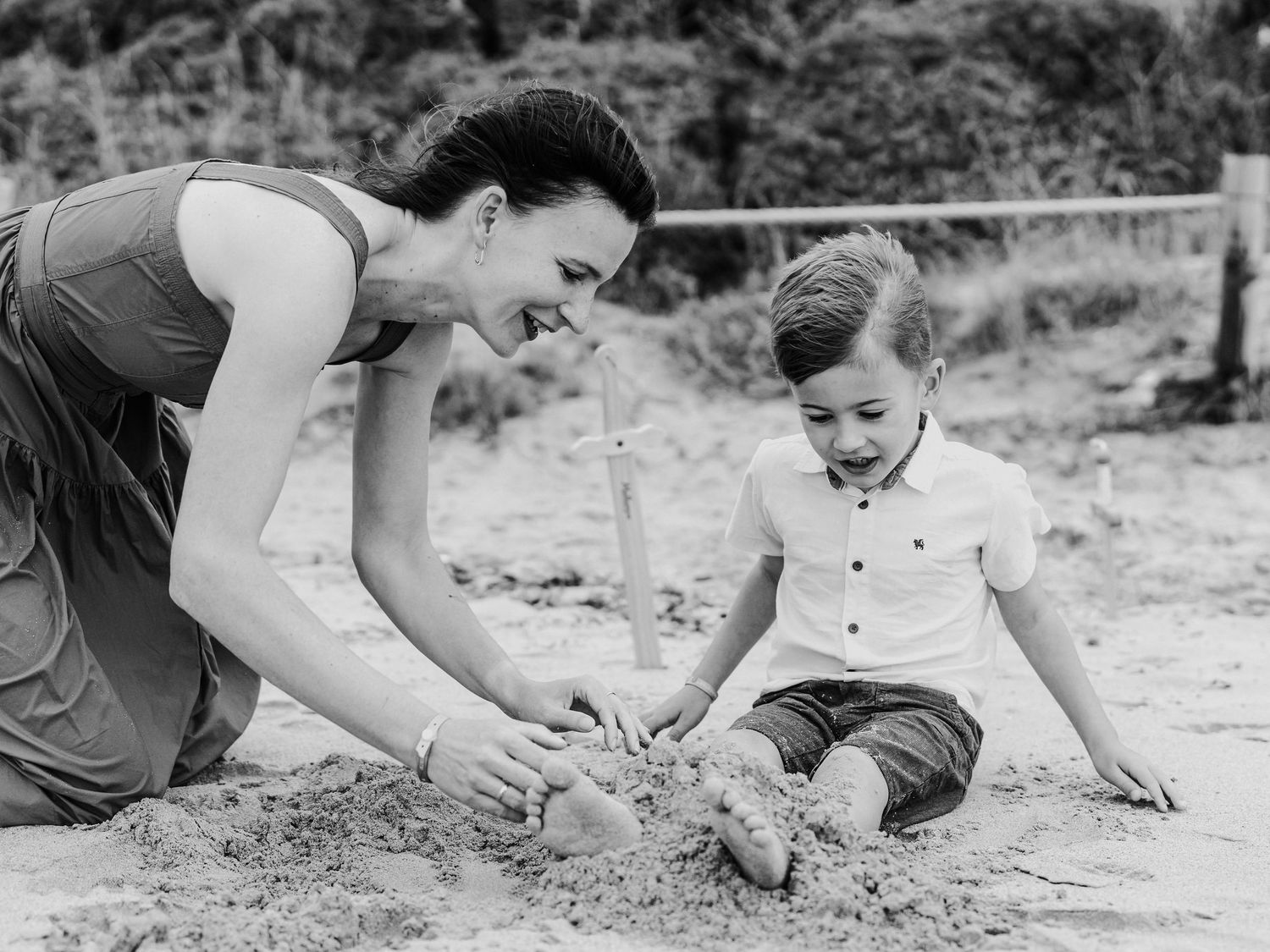 Black and white photo of mother and young son playing in sand on beach.