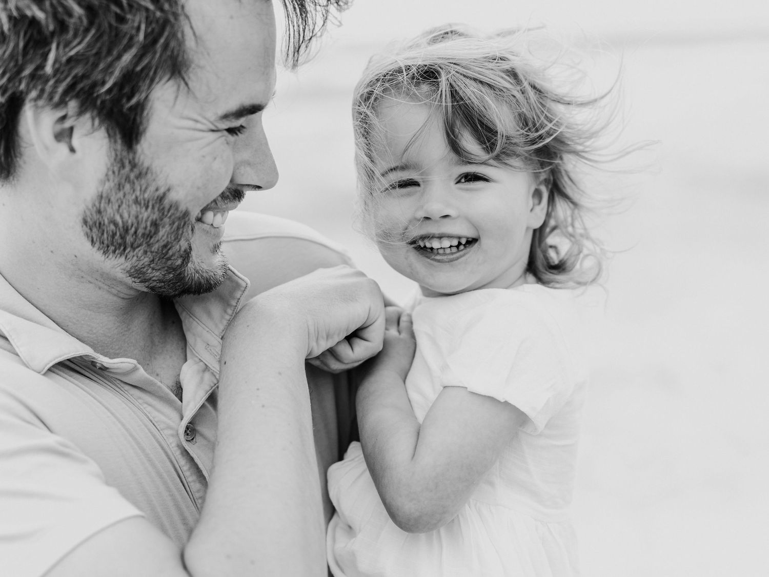 Black and white photo of father and laughing toddler girl at beach.