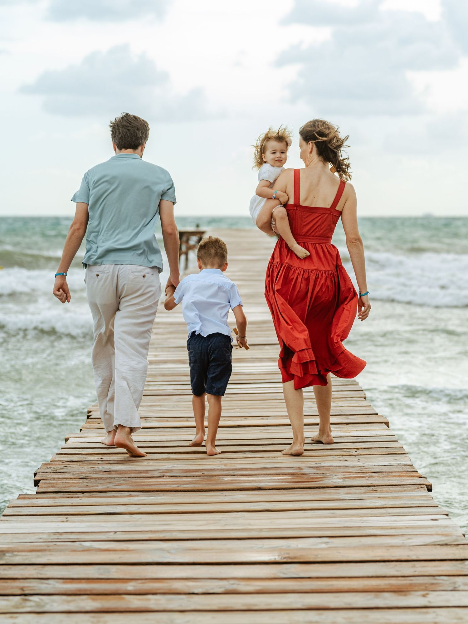 Family walking together on a seaside pier in windy weather, candid family photography by Herzenshaus Studio, Frankfurt Rhein-Main.
