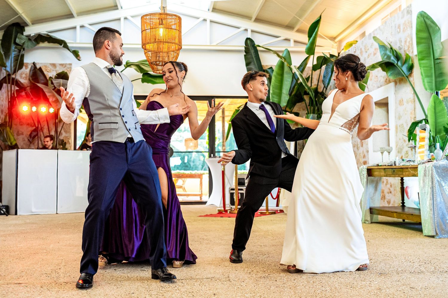 Two couples dance together at a wedding reception, wearing formal attire including a purple gown and white bridal dress.