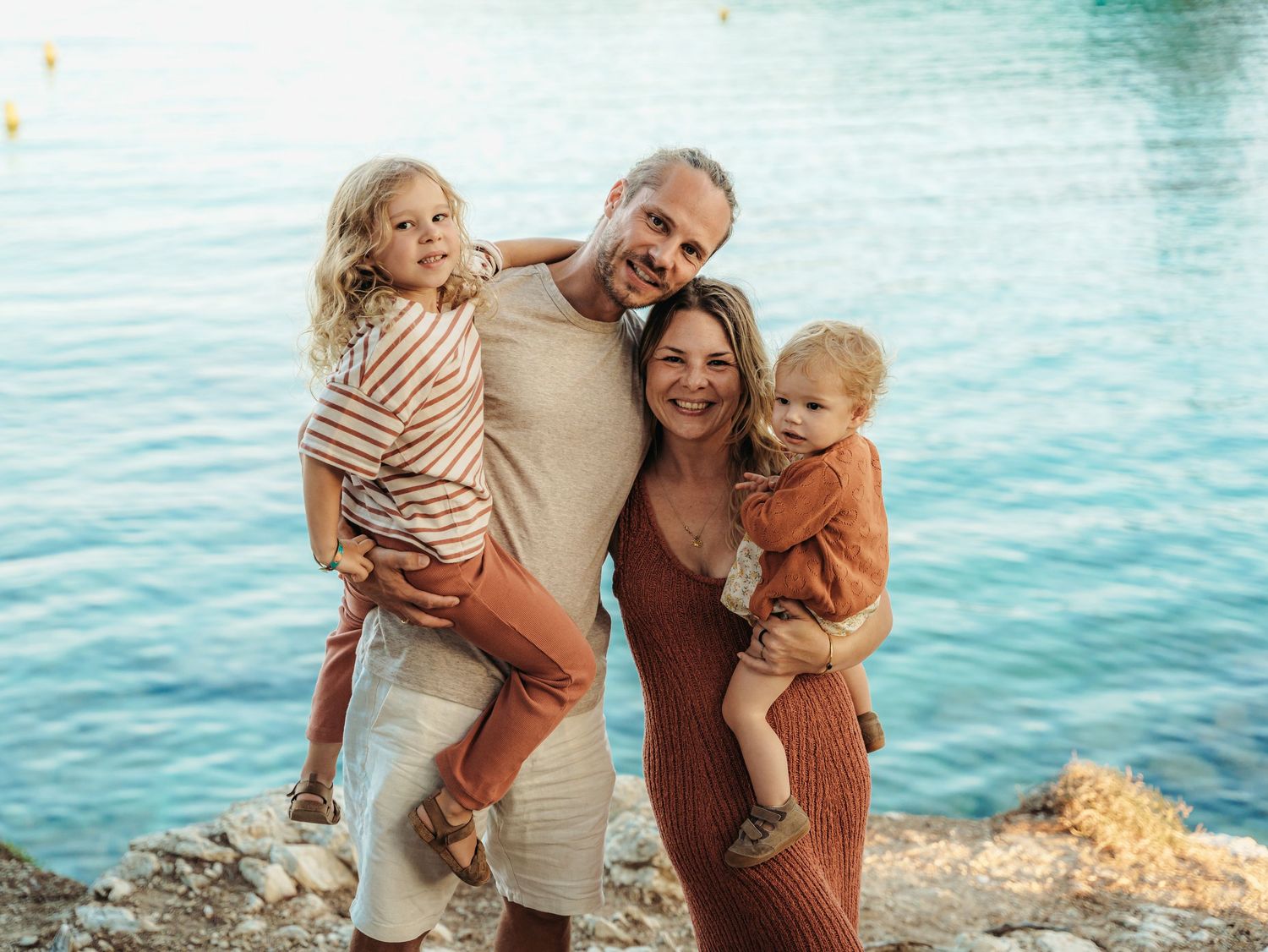 Happy family of four posing together by sparkling turquoise coastal waters.