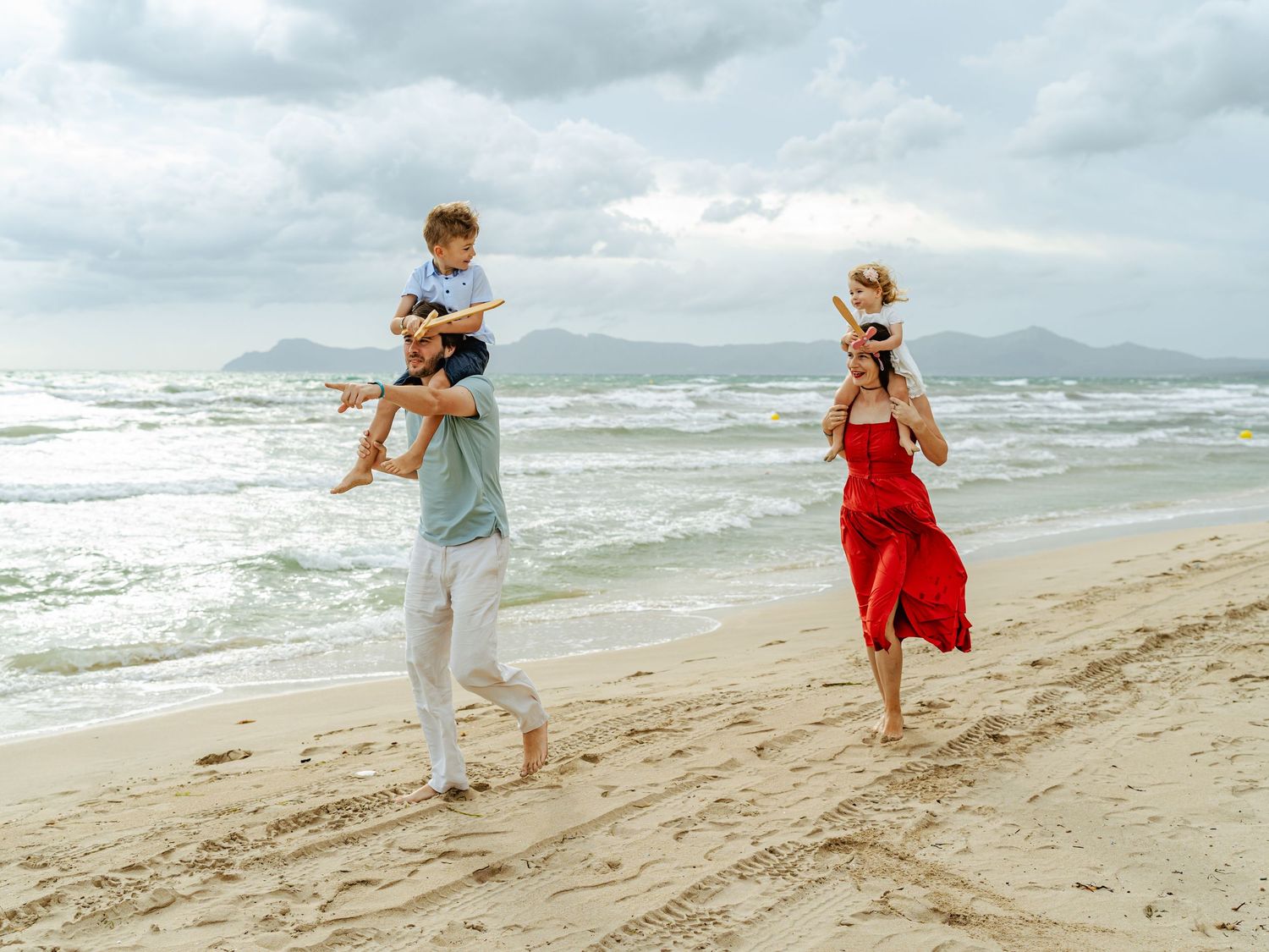 Joyful family of four playing on beach, father lifting son while mother carries daughter.