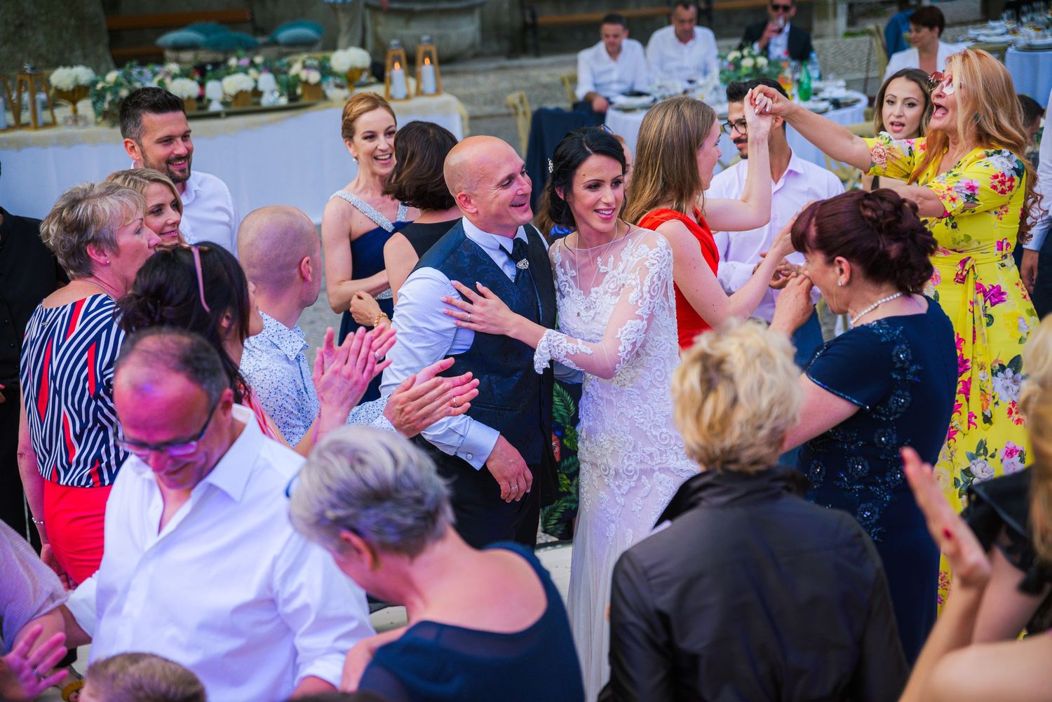 Bride and groom celebrate joyfully surrounded by cheering wedding guests on the dance floor.