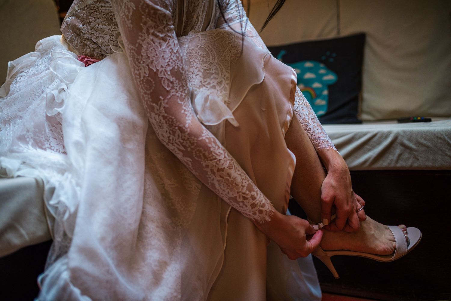 Bride in lace wedding dress putting on heels while seated before ceremony.
