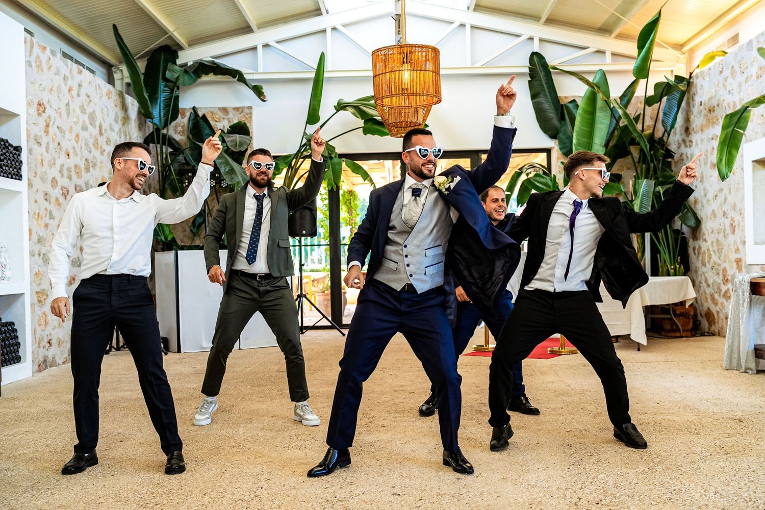 Groom and groomsmen strike fun energetic dance poses together at a tropical wedding reception venue.