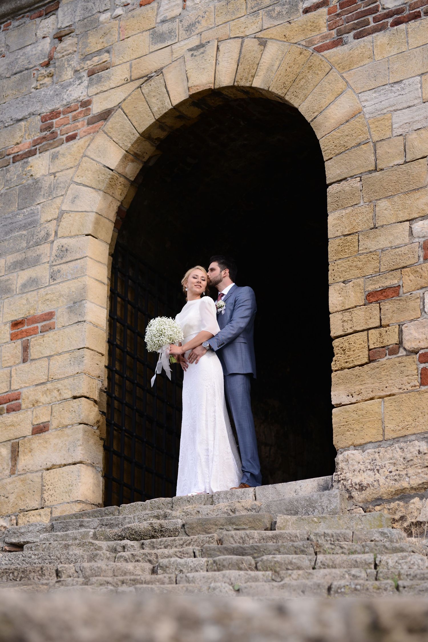 Bride and groom embracing beneath a historic stone archway, timeless documentary wedding photography in Germany