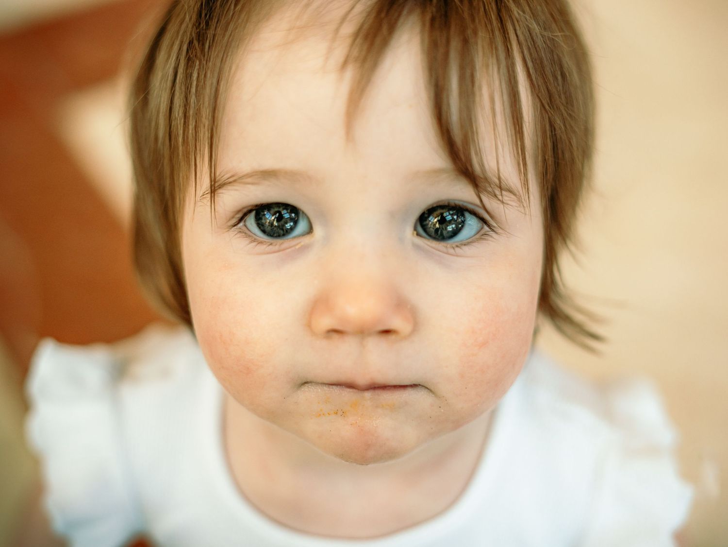 Close-up portrait of cute toddler girl with blue eyes and freckles in white top.