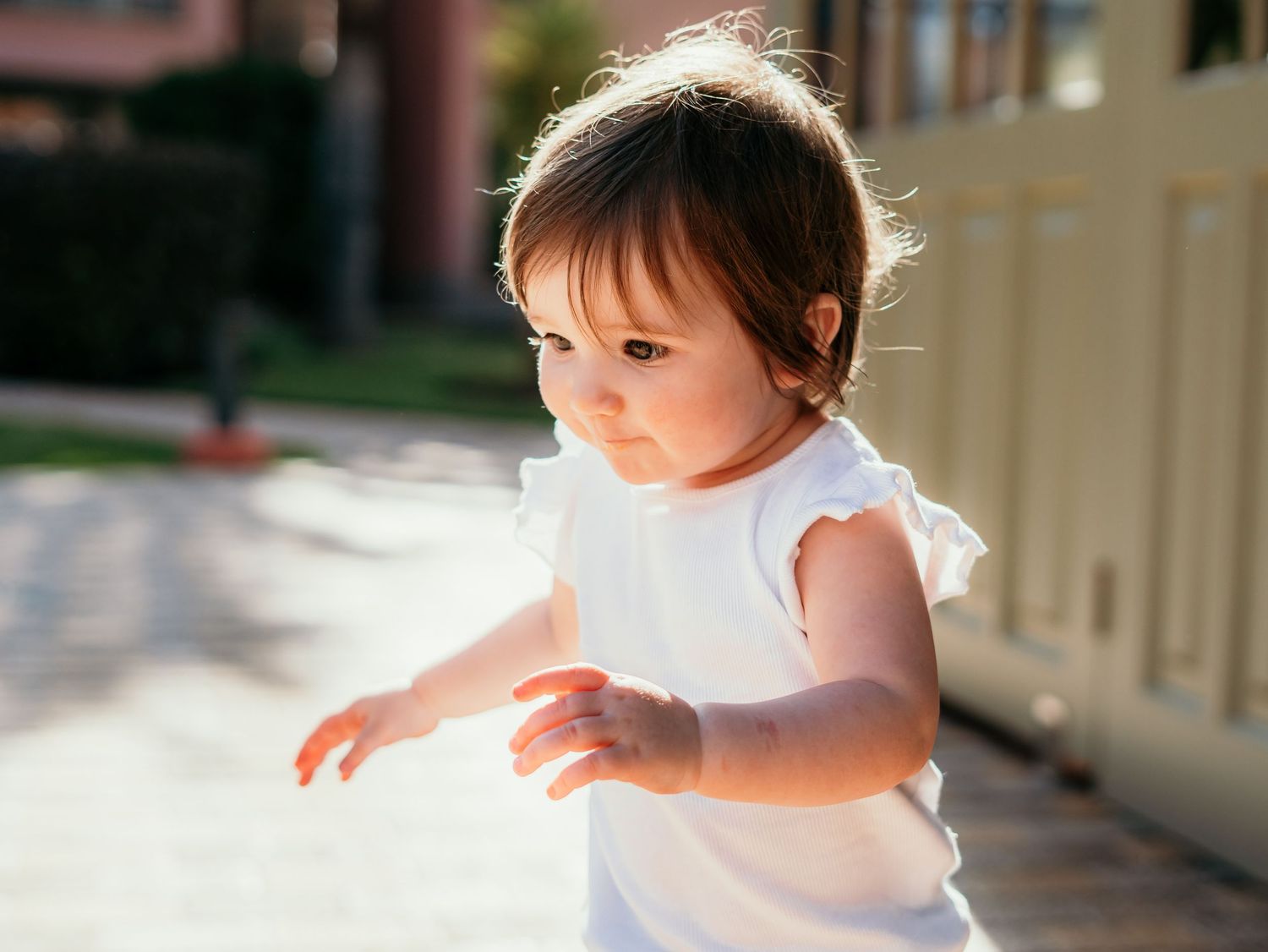 Adorable toddler girl in white ruffled top walking outdoors in warm golden sunlight.