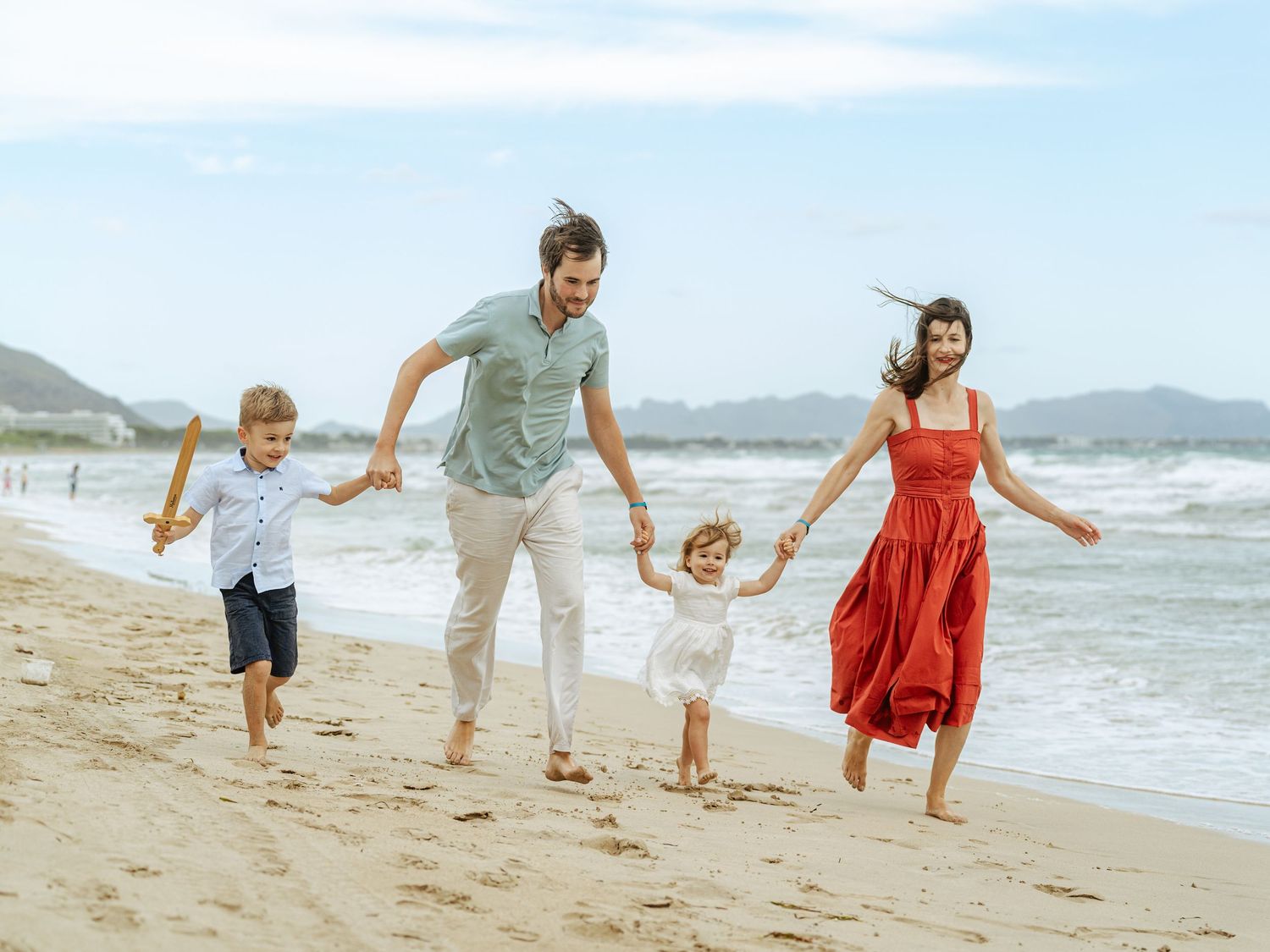 Cheerful family of four holding hands and running along a sandy beach.