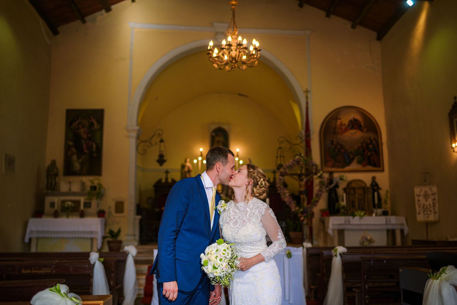 Bride and groom share a kiss inside a charming church decorated with flowers and religious artwork.