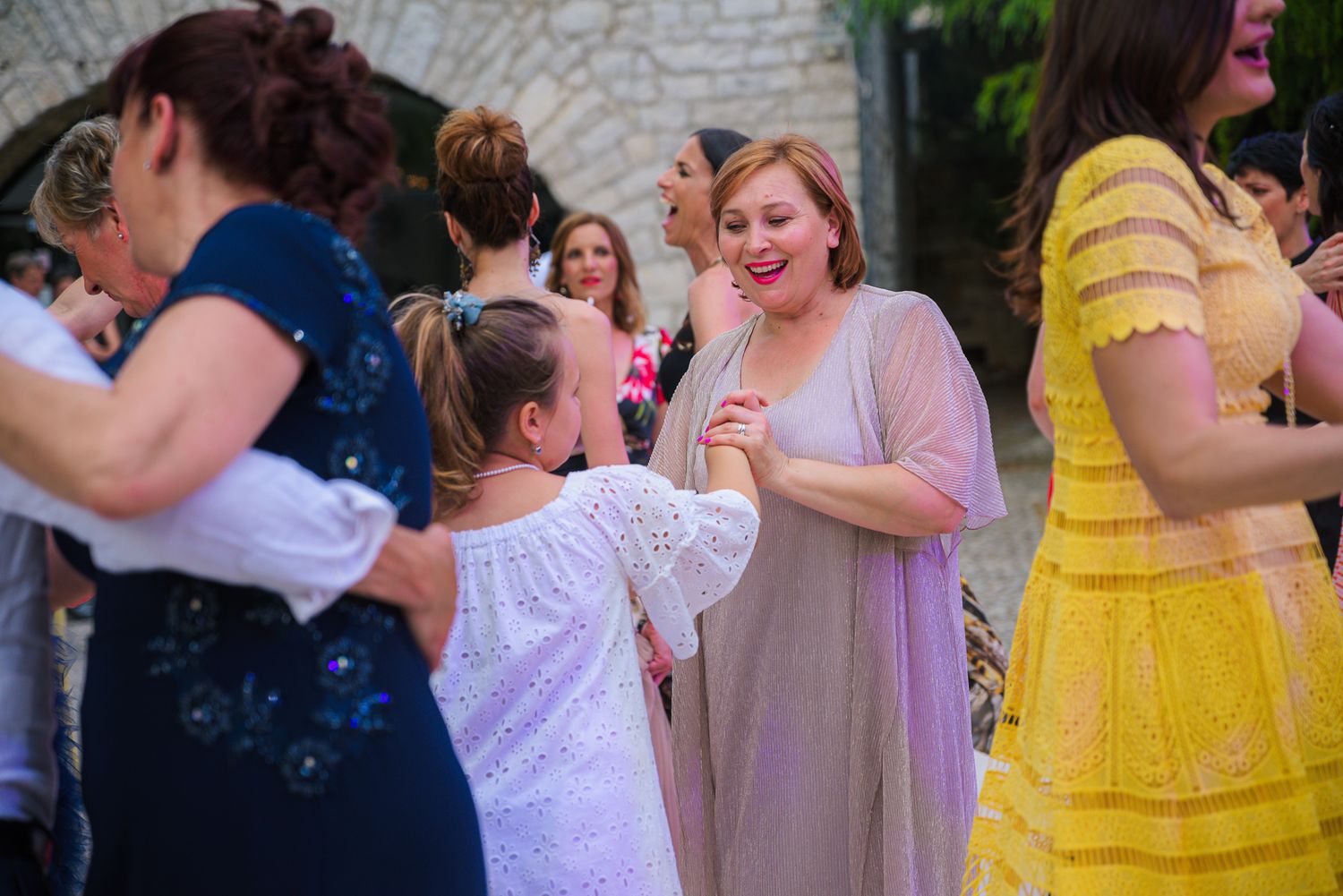 Woman in pink dress dancing with young girl at outdoor wedding celebration.