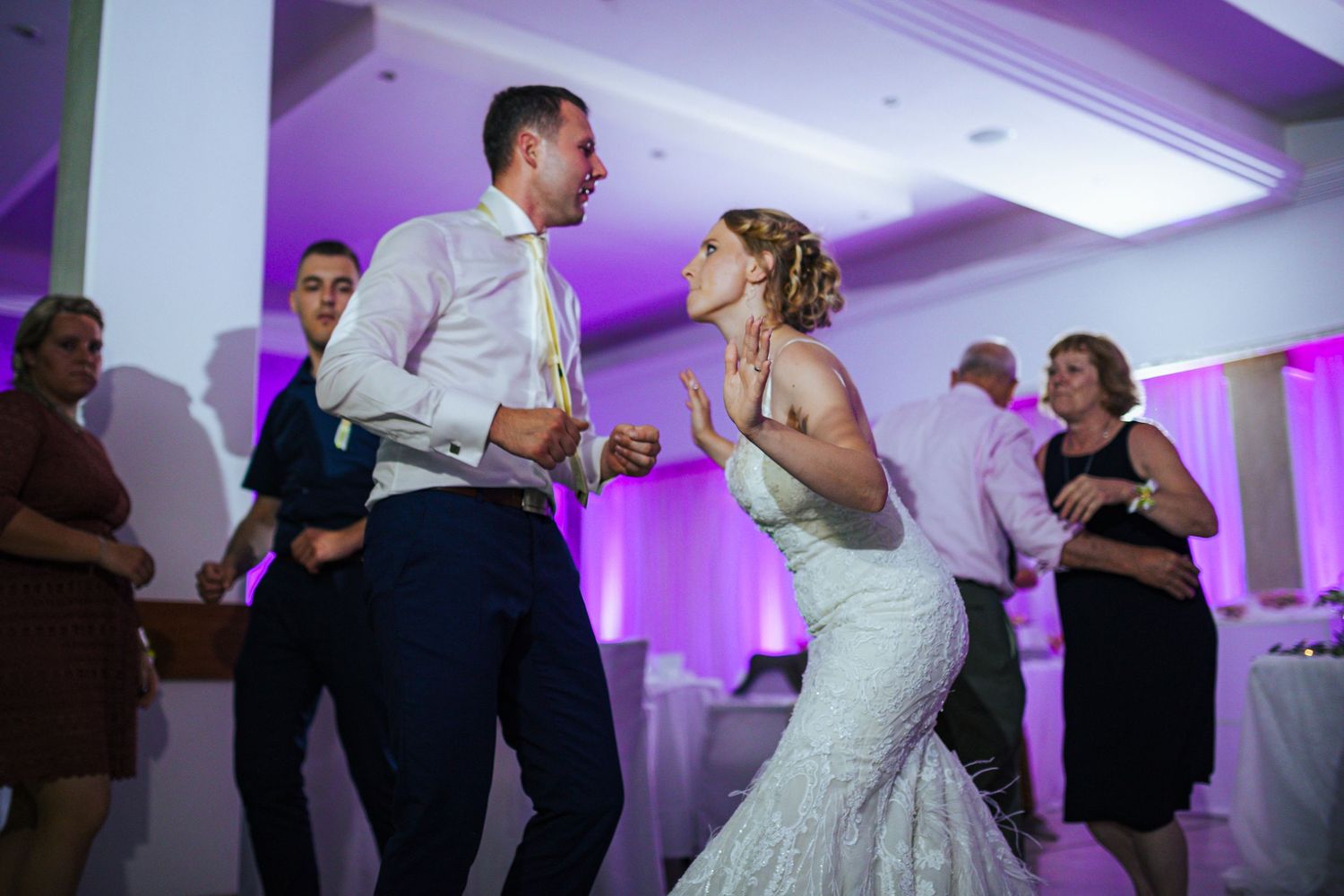Bride and groom dance energetically together surrounded by guests at wedding reception.