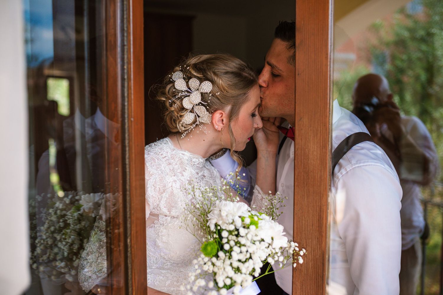 Bride and groom sharing a kiss in doorway, bride holding white floral bouquet.