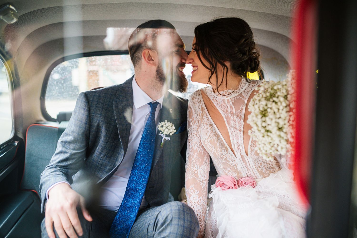 Bride and groom sharing a tender kiss inside a vintage black taxi cab on their wedding day.
