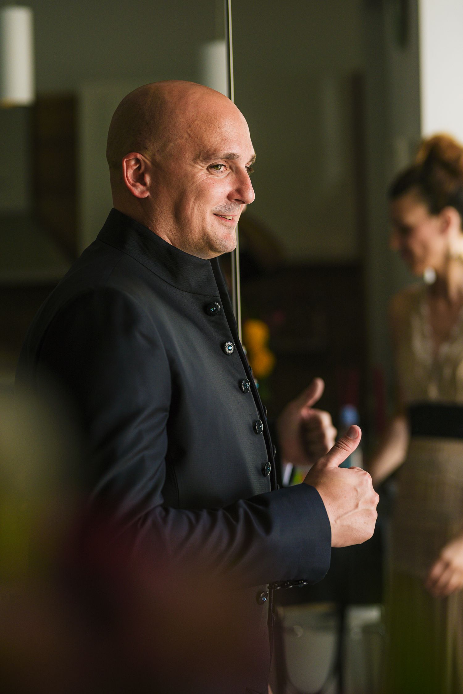 Smiling bald groom in black mandarin collar jacket posing before wedding ceremony.