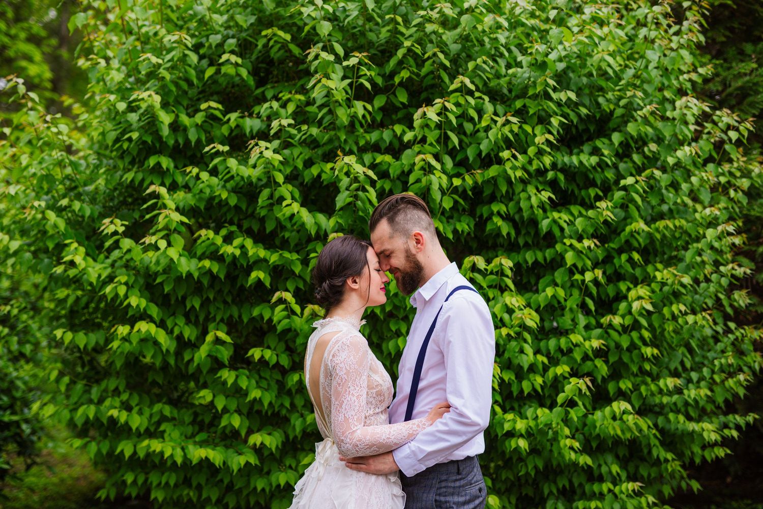 Bride and groom sharing an intimate wedding portrait surrounded by lush green foliage. Intimate weddings by Herzenshaus Studio, Frankfurt.