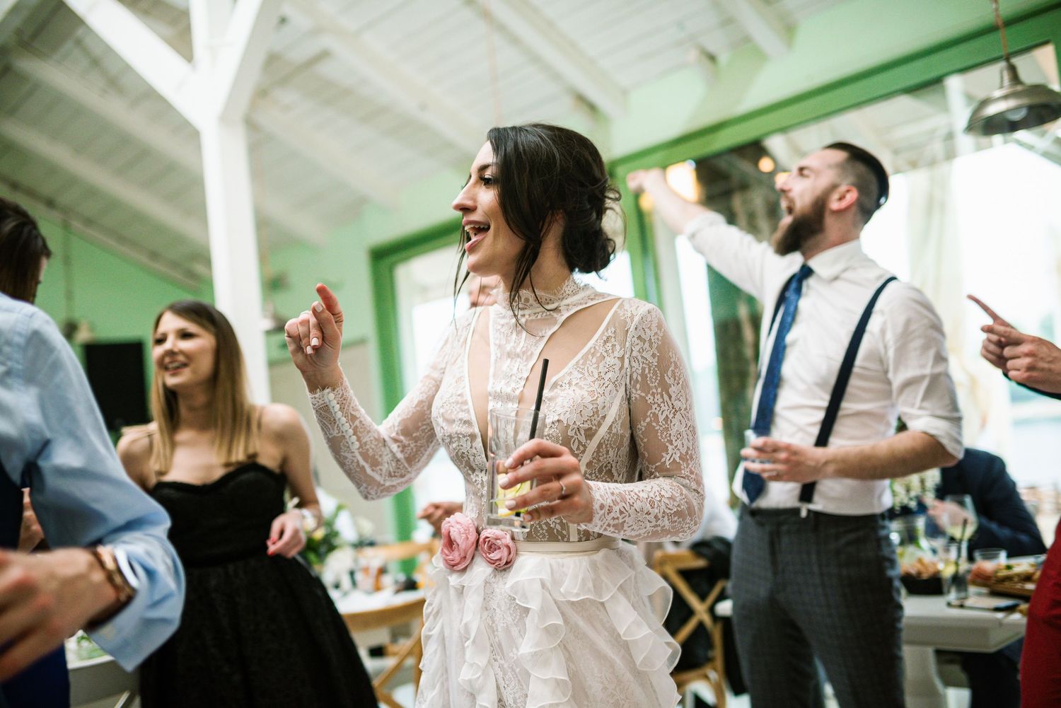 Bride in lace wedding dress laughing and dancing joyfully with guests at wedding reception.