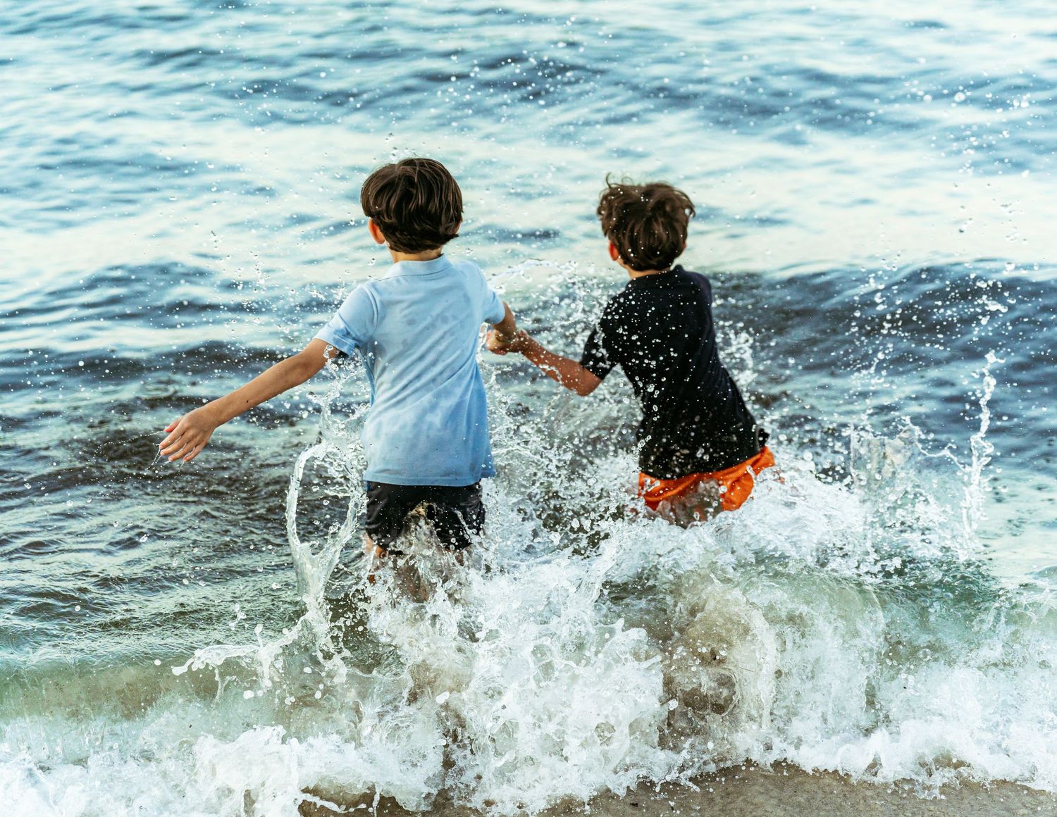 Two boys splashing and playing in ocean waves on a sunny beach day.