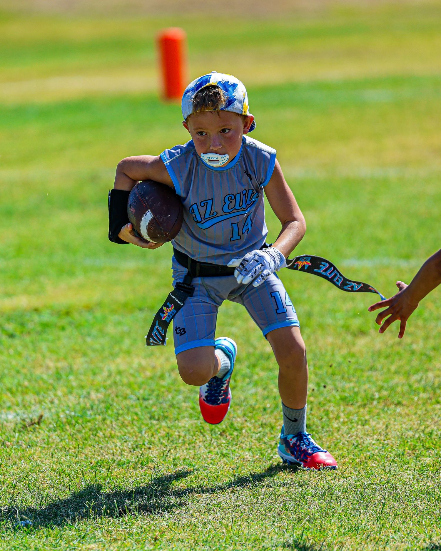A young boy in blue flag football uniform runs with the ball during a youth league game.