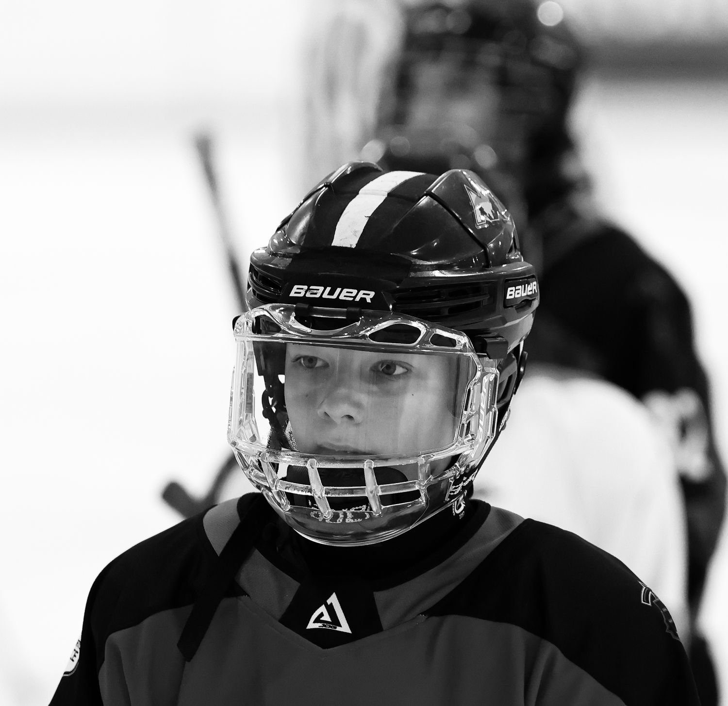 Close-up black and white portrait of young hockey player wearing Bauer helmet and face shield.