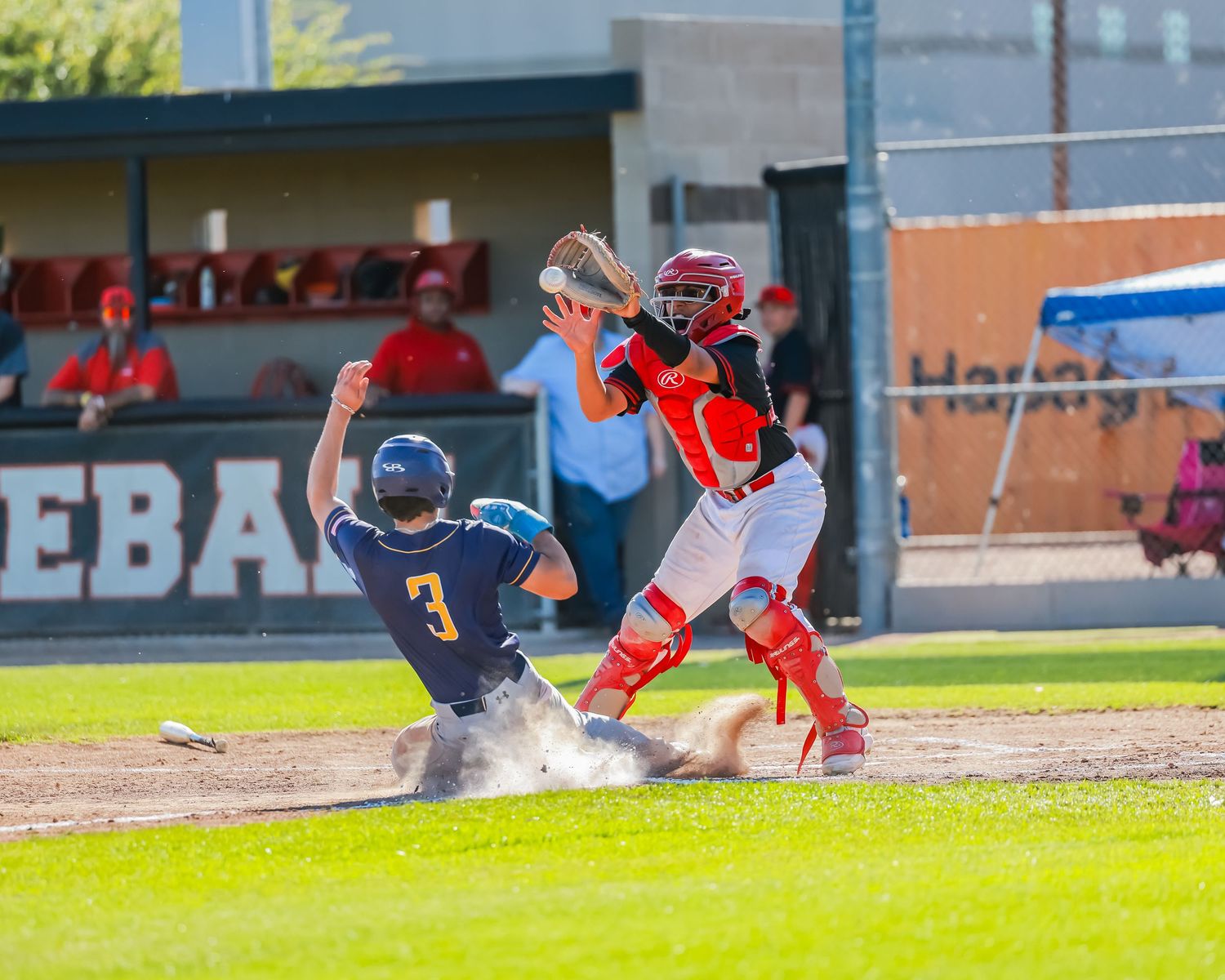 Baseball catcher in red gear attempts tag as runner slides into home plate.