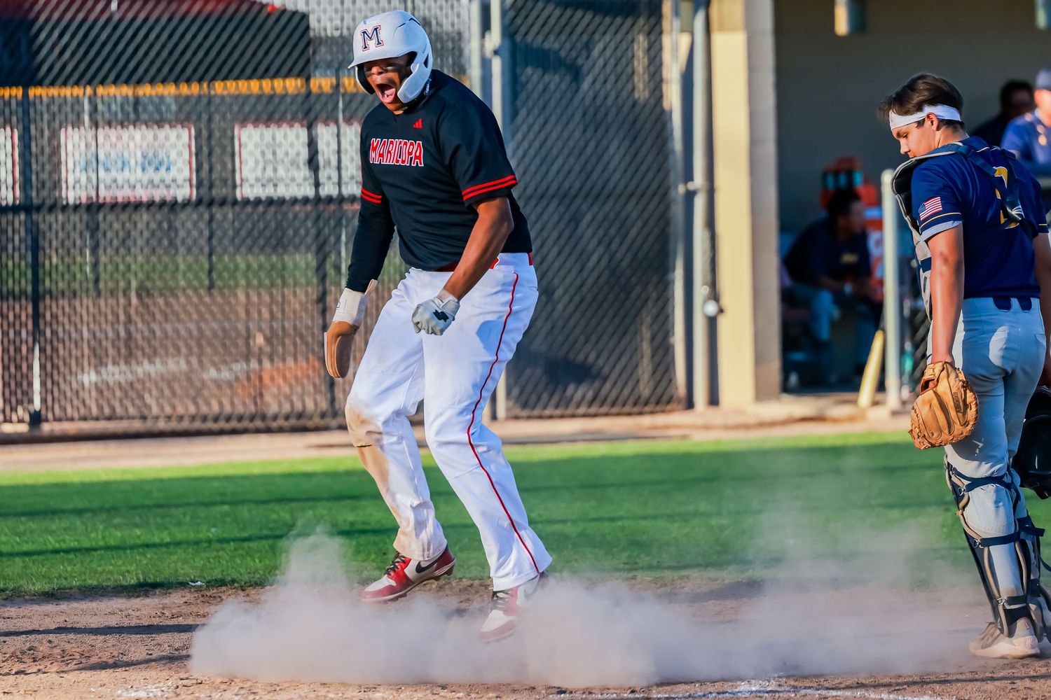 Baseball player stomps home plate in cloud of dust during daytime game with catcher nearby.