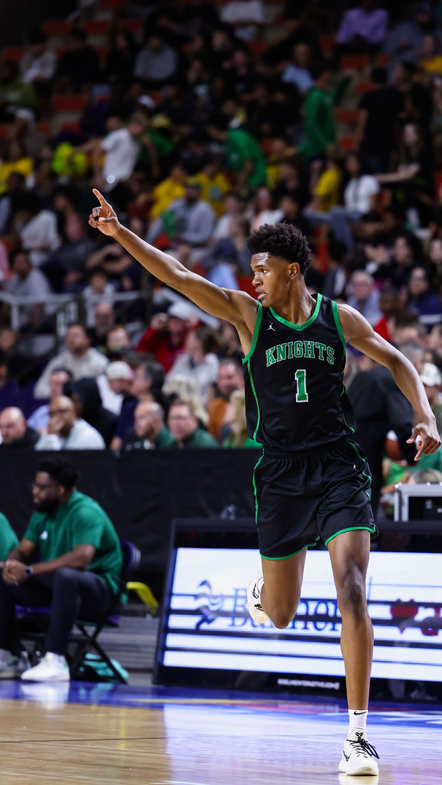 Knights basketball player number 1 in black and green uniform pointing during a crowded arena game.