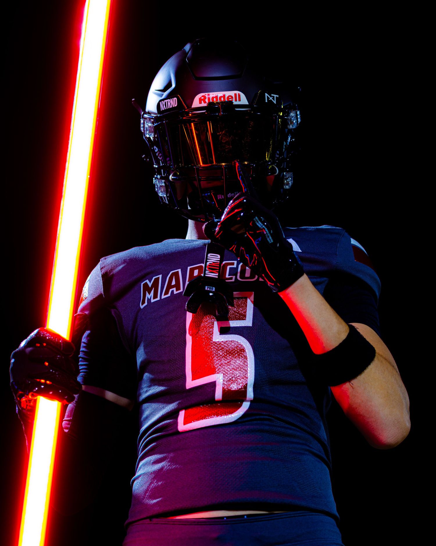 Football player in Madison number 5 jersey holds glowing red light saber.