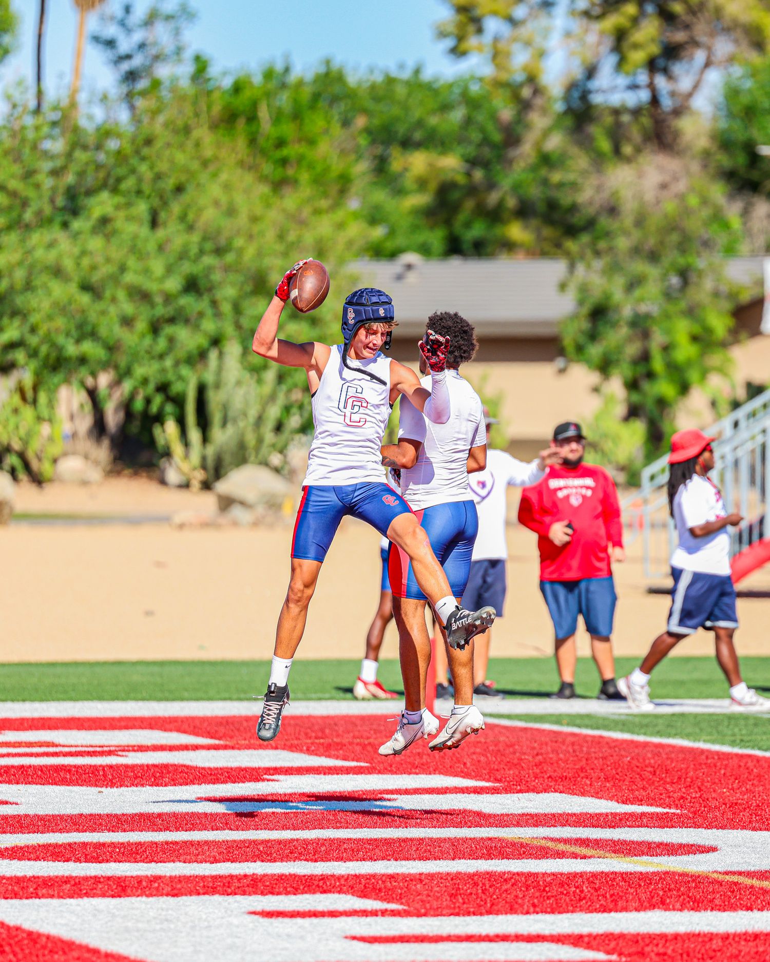 Youth football players celebrate a touchdown in the red end zone during a summer practice.