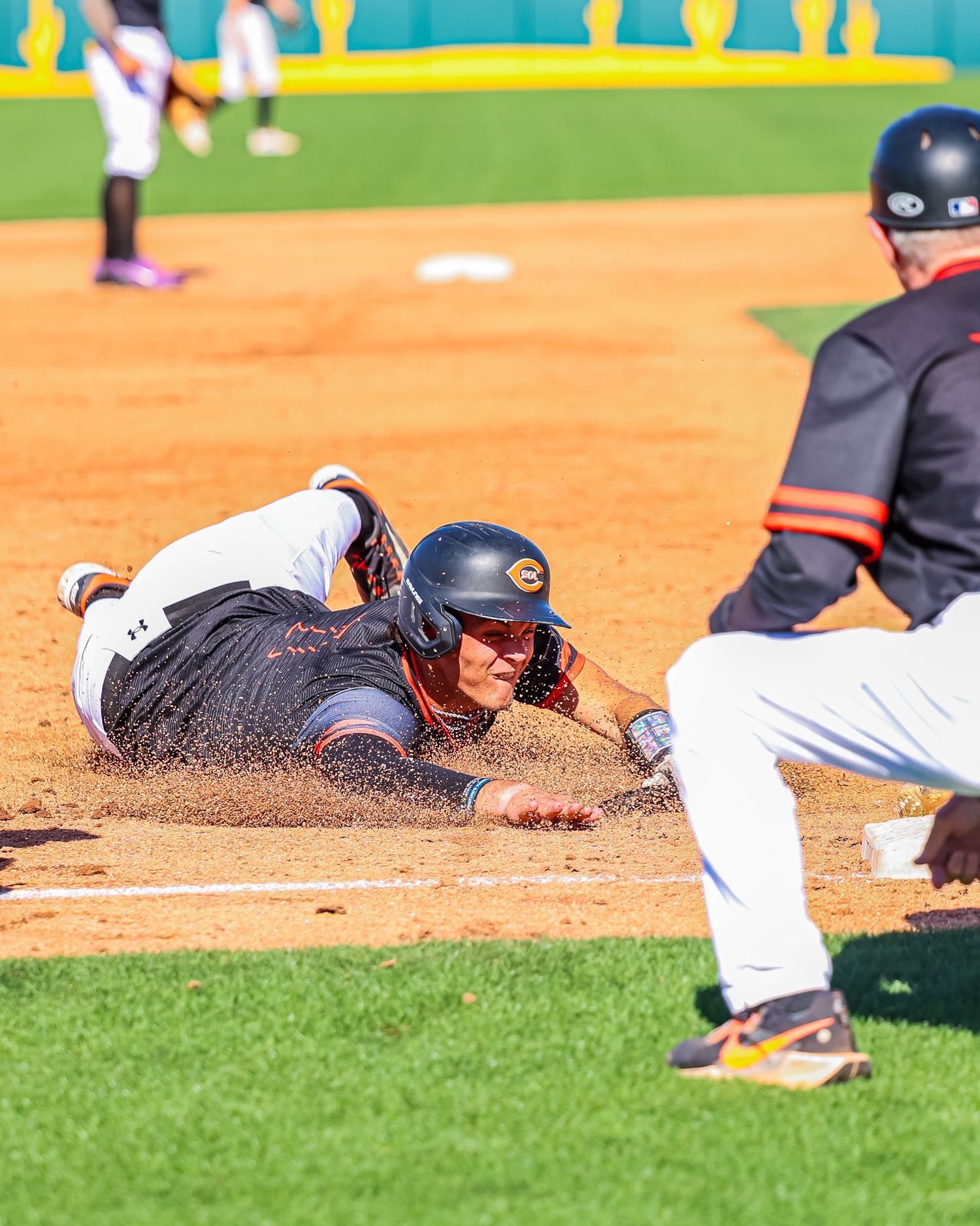 Baseball player slides into base in cloud of dirt as fielder reaches for the tag.