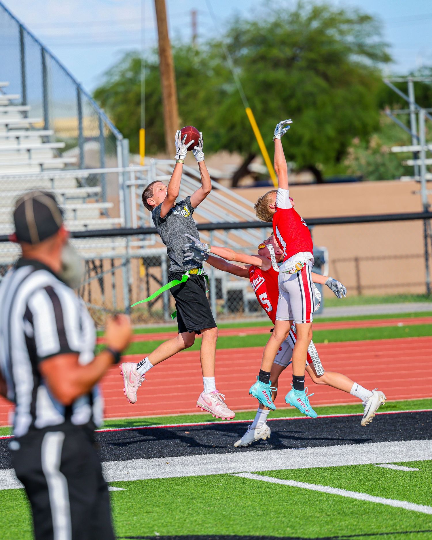 Two players jump for a football catch in the end zone as a referee watches during a flag football game.