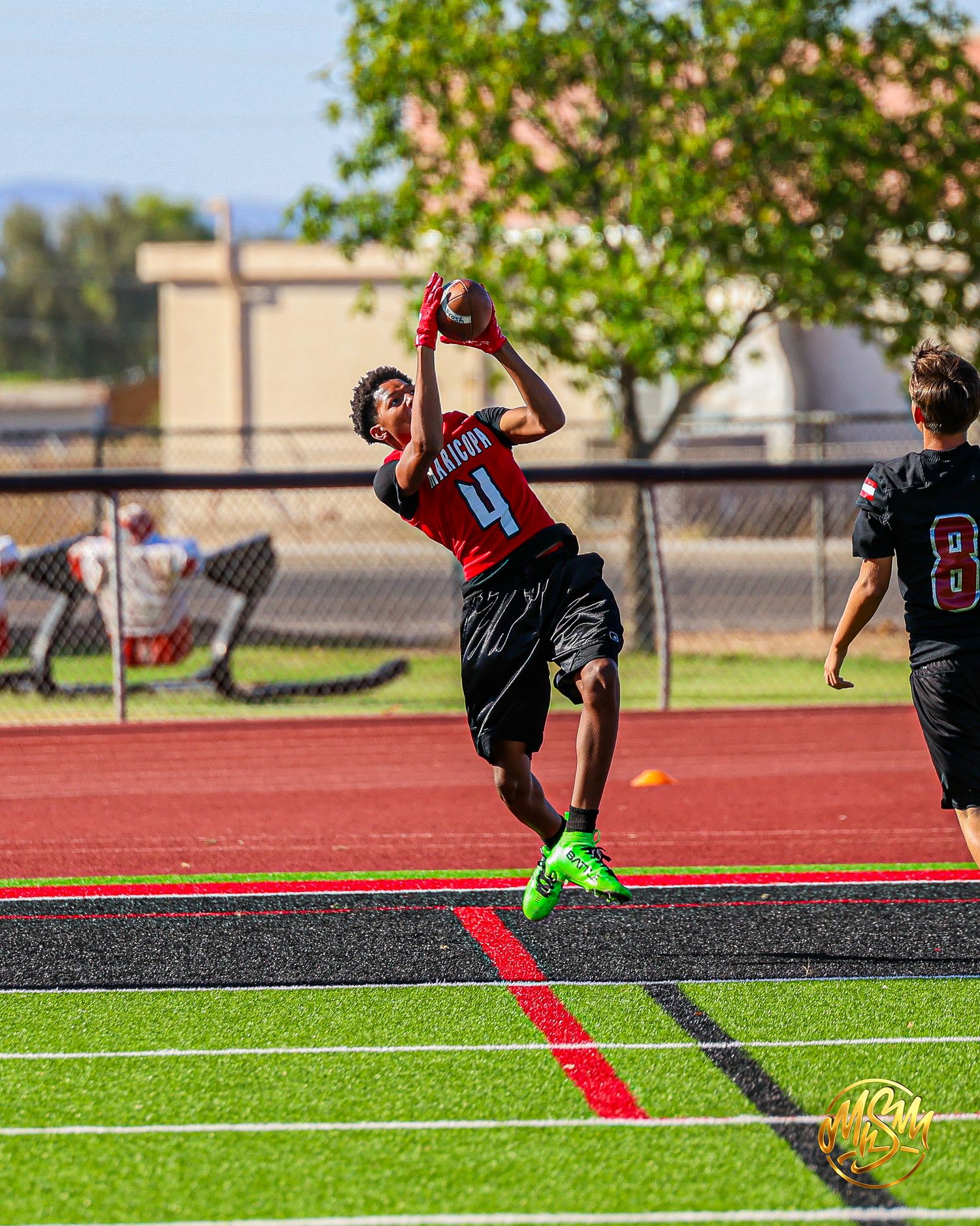 Youth football player #4 leaps to make catch on red turf field during game.