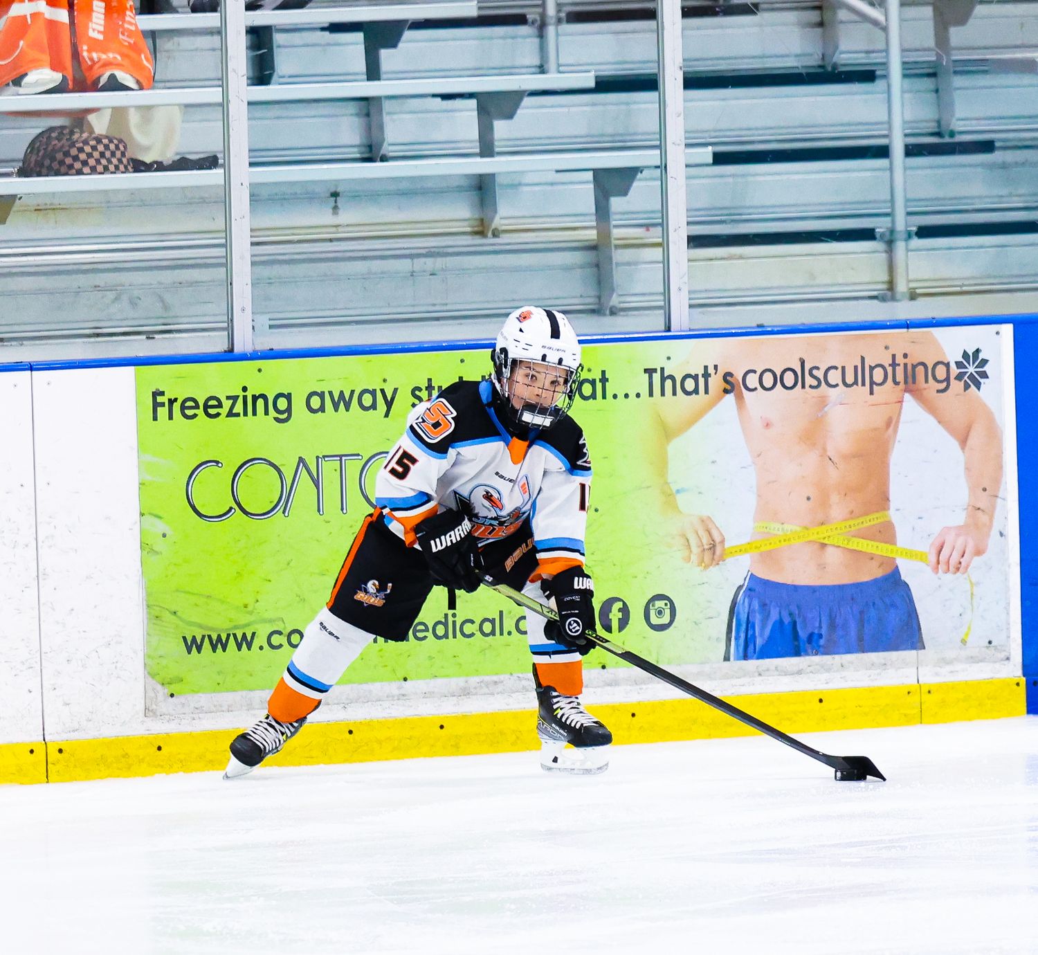 Ice hockey player number 5 in orange and white uniform skating with puck along the boards.